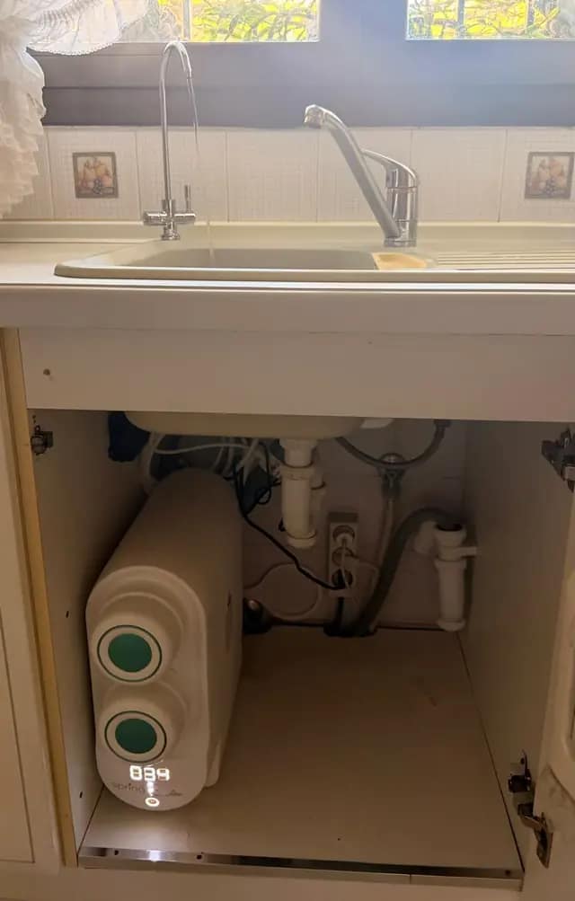 Spring 2.0 blanca instalada por Tu Calidad bajo el fregadero de una cocina, con el grifo de agua pura sirviendo agua junto al grifo de siempre